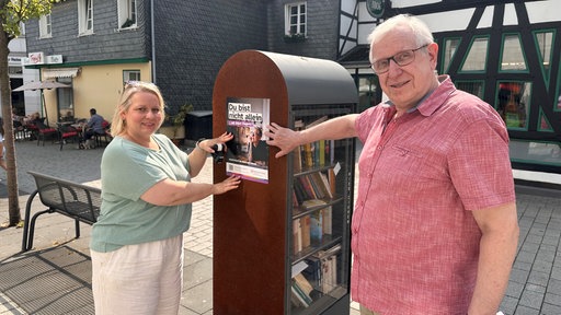 Eine Frau und ein Mann halten je eine Hand auf ein Plakat