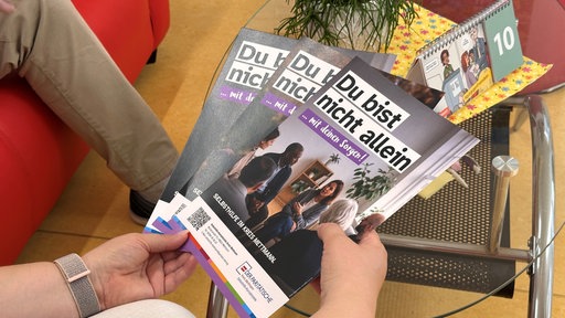Eine Hand hält drei verschiedene Flyer in der Hand
