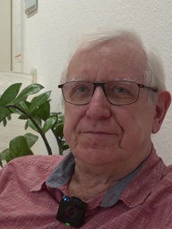 Ein Mann mit Brille sitzt vor einer grünen Pflanze und lächelt