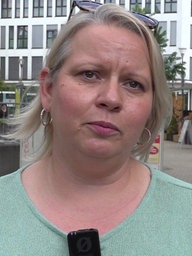 Eine Frau mit blonden Haaren und Ohrringen blickt nachdenklich 