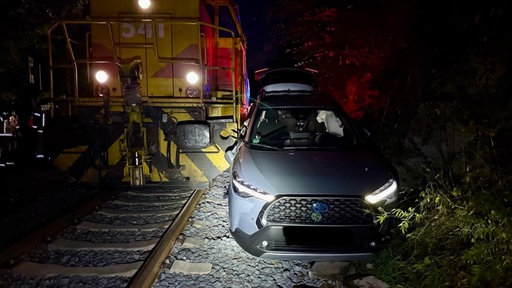 Ein Auto steht zerbeult neben einem Zug. Unfall am Bahnübergang Auermühle
