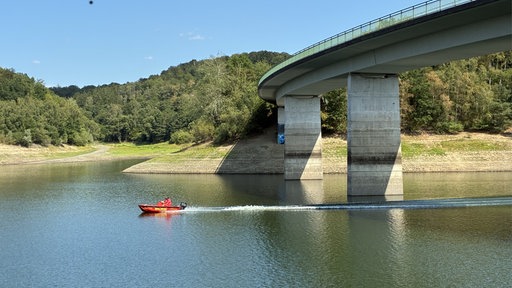 Rotes Boot auf dem Wasser vor einer Betonbrücke 