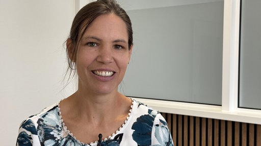 Eine junge Frau mit dunklen Haaren lächelt in die Kamera.