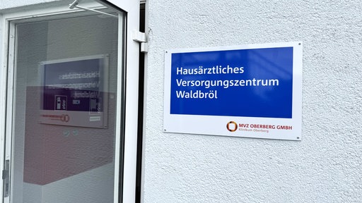 Ein blau-weißes Schild am Eingang des MVZ Oberberg GmbH mit der Aufschrift „Hausärztliches Versorgungszentrum Waldbröl“.