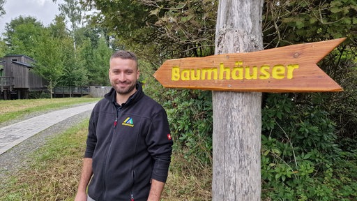 Ein Mann steht vor einem Wegweiser zu den Baumhäusern.