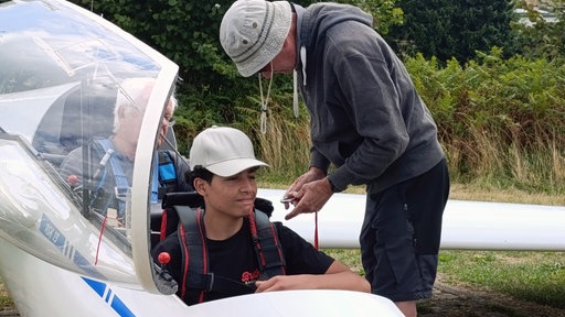 ein Schüler steugt in ein Segelflugzeug ein und wird angeschnallt