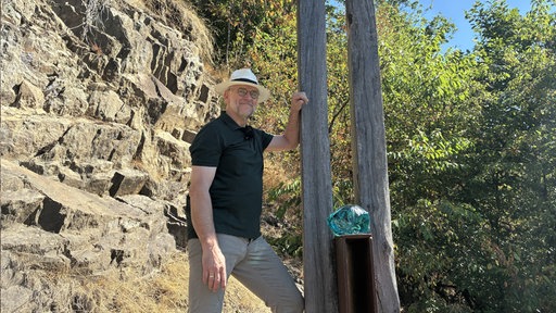 Ein Mann steht vor einem Holzkunstwerk. 