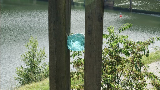 Eine türkise Glaskugel steckt zwischen zwei Holzpfählen. 