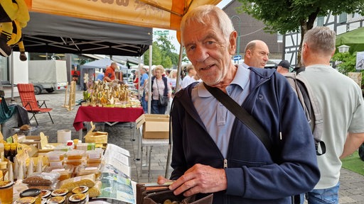 Ein Mann steht an einem Marktstand und öffnet eine Geldbörse.