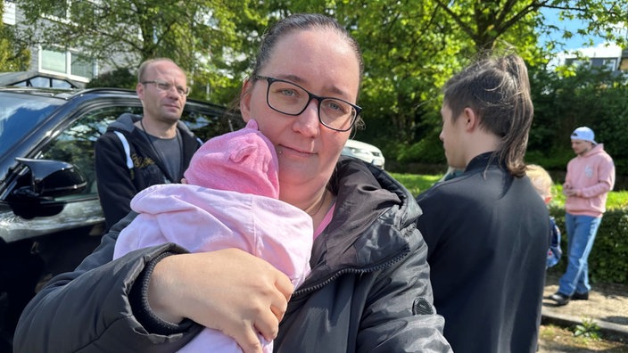 Eine Mutter mit einem Baby auf dem Arm guckt in die Kamera