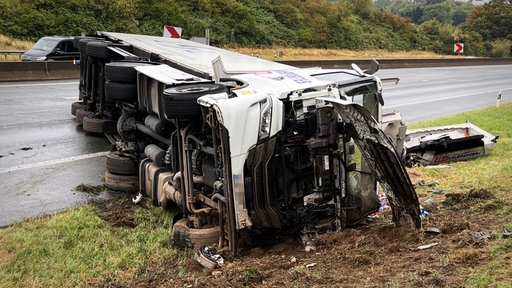 Ein Lkw liegt seitlich auf Fahrbahn und Grünstreifen.