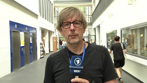 WDR Reporter Wolfram Lumpe steht mit Mikrofon auf dem Flur des Gerichtsgebäudes