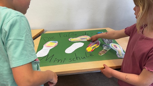 Kinder stehen vor einem grünen Plakat, auf dem bunte Fußabdrücke draufgeklebt sind