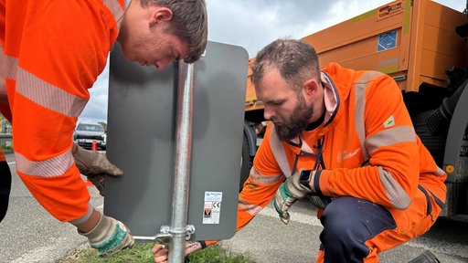 Zwei Straßenwärter der A4 in orangenen Arbeitsjacken