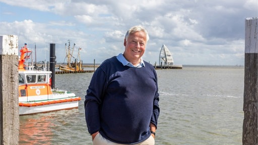 Ein Mann steht lächelnd im Hafen einer Insel. 