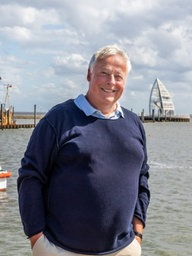 Ein Mann steht lächelnd im Hafen einer Insel. 