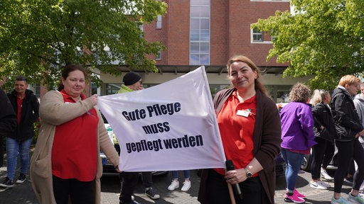 Zwei Frauen die ein Banner halten auf dem steht: "gute Pflege muss gepflegt werden"