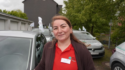 Eine Frau steht vor mehreren Autos mit Fahnen