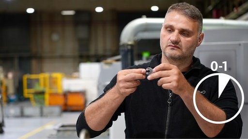 Ein Mann steht in einer Maschinenhalle und inspiziert ein Werkzeug, das er in seiner Hand hält.