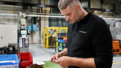 Ein Mann steht in einer Werkstatt und hält einen Steckschlüsselsatz in der Hand, den er anschaut.