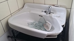 ein kaputtes Waschbecken, in dessen Becken Glas- und Keramikschreben liegen