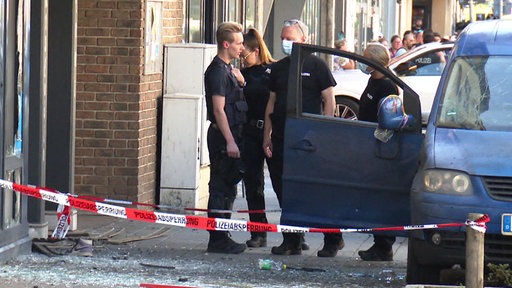 Zivil Polizisten stehen am Tatort. Glassplitter auf Bürgersteig und Absperrung.
