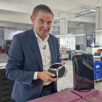Ein Mann hält einen Mercedes-Stern in der Hand, daneben steht eine verchromte Schutzhülle für die Playstation.