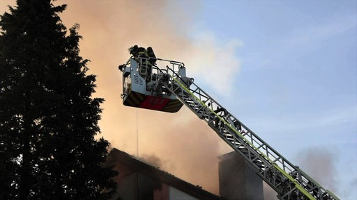Eine Feuerwehrperson steht im Korb einer Drehleiter, hinter ihr eine Rauchwolke