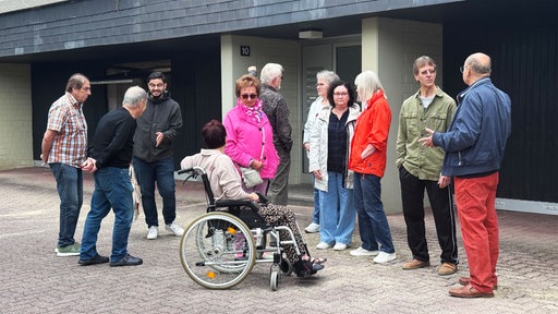 Elf Menschen stehen vor einem Gebäude und unterhalten sich.
