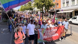 Protestmarsch. Banner liest "Zusammen Vielfalt Verteidigen"