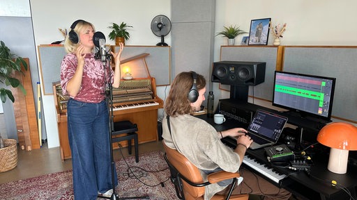 Leonora singt in ein Mikrofon, ihr Produzent sitzt am Laptop