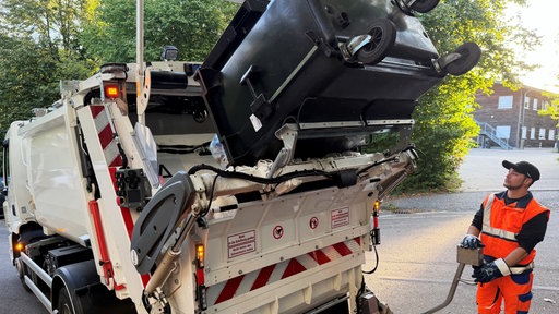Ein Müllwerker leert einen Container in ein Müllfahrzeug aus