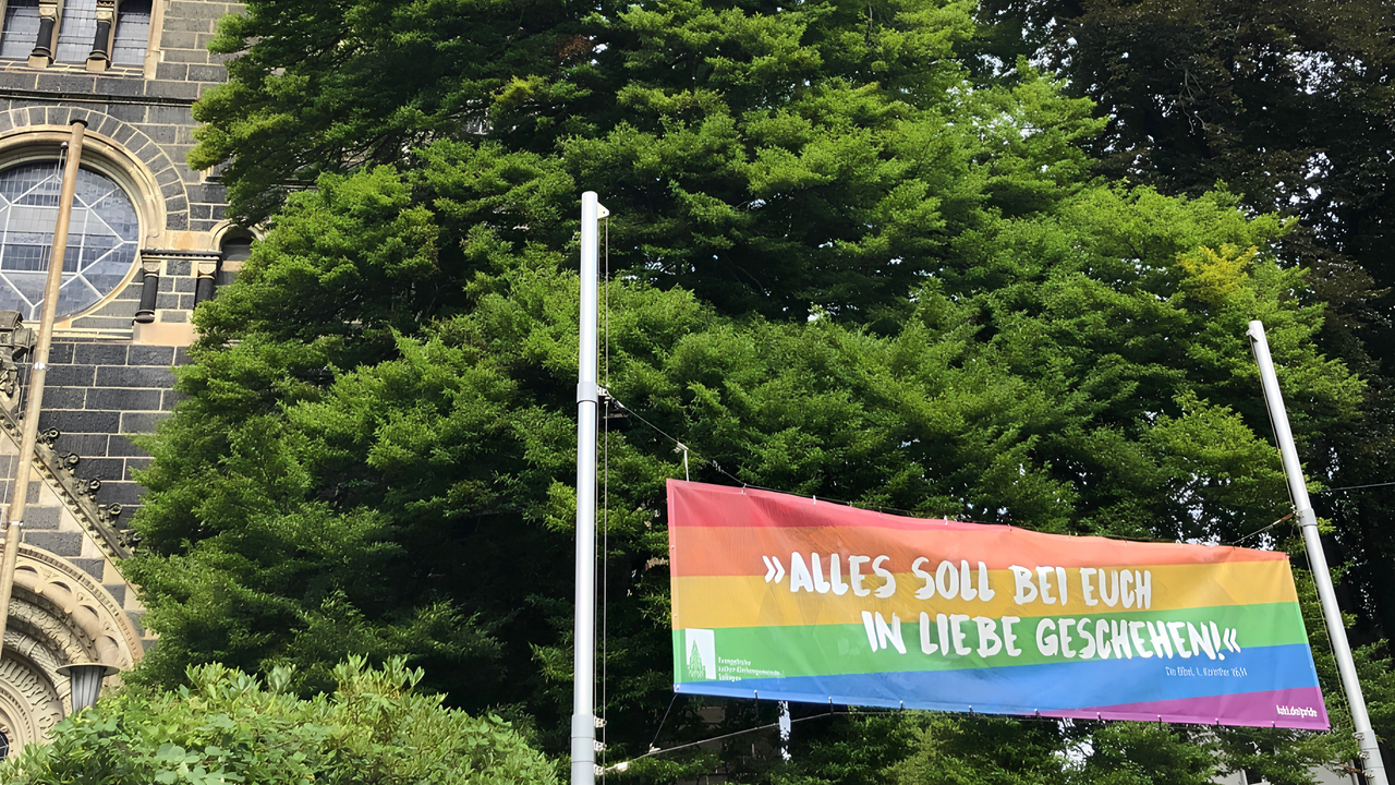 Eine Regenbogenflagge vor der Lutherkirche in Solingen auf der steht "Alles soll bei euch in Liebe geschehen."