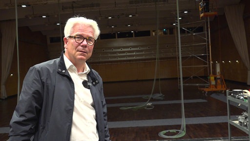 Mann mit weißen Haaren und Brill im Hintergrund der Konzertsaal