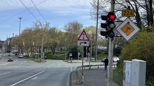 Straßenkreuzung mit roter Ampel, Verkehrsschildern und Gehweg an einer breiten Straße