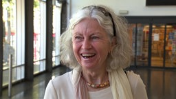 Eine lachende ältere Frau mit schulterlangen blonden Haaren.