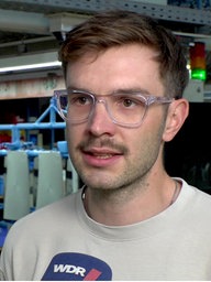 Ein Mann steht in einer Firmenhalle vor einem WDR-Mikro