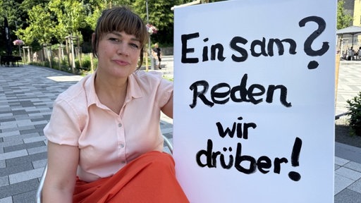 Eine Frau hält ein Schild auf dem steht: "Einsam? Reden wir drüber!"