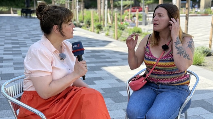 Frau mit orangenem Rock spricht mit Frau mit buntem Top