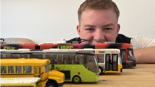 Mann schaut auf Modellbusse, die auf einem Holztisch stehen