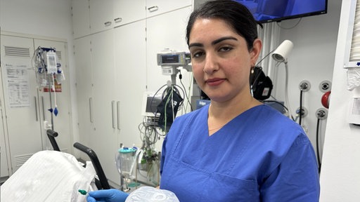 Eine Gesundheitspflegerin im blauen Kasack steht in einem OP-Saal.