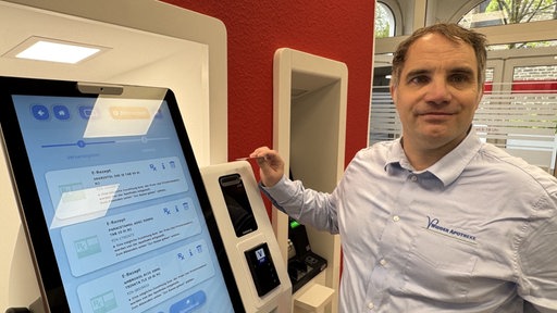Mann neben Bankautomat schaut in die Kamera