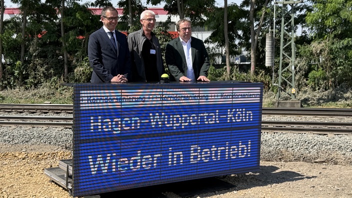drei Männer mit Bahnanzeige