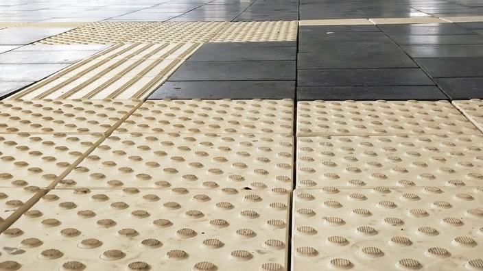 Dunkelgraue Bodenfliesen und beige Bodenplatten mit vielen kleinen runden Noppen.