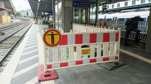 Das Bild zeigt einen Bahnsteig eines Bahnhofs, auf dem ein Bereich wegen Bau- oder Wartungsarbeiten abgesperrt ist.