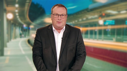 Ein Mann mit Brille steht vor einem Hintergrund, wo Bahnen zu sehen sind