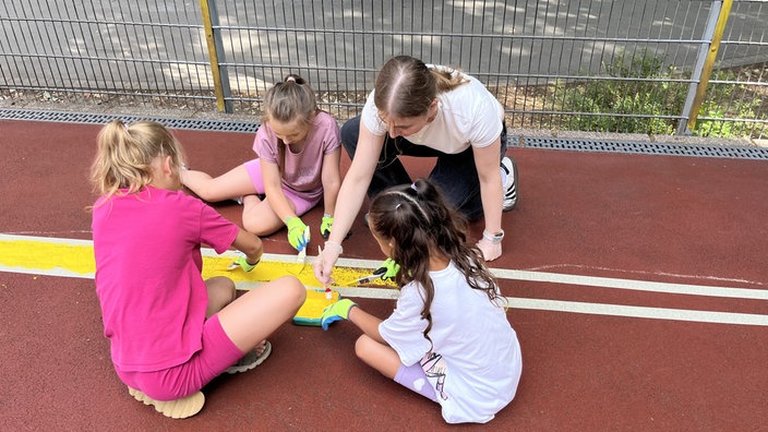 Drei Kinder und eine Frau färben eine Völkerballfeldmarkierung gelb
