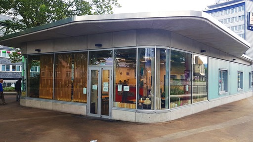 Das Bild zeigt einen Pavillon mit einem Flachdach und einer an den Gebäudeecken abgerundeten Glasfront.