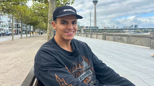 Ello sitzt auf einer Bank auf der Rheinpromenade