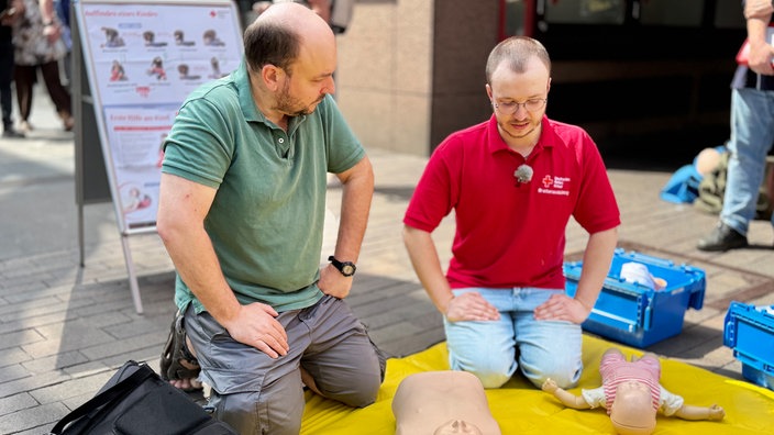 Ein Sanitäter erklärt einem Interessenten die Rettungspuppe